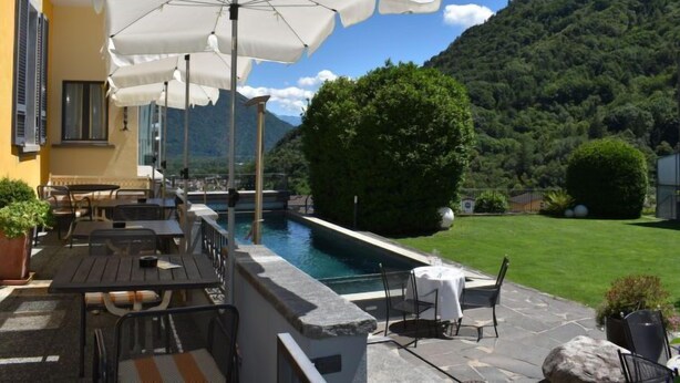 Un espace de restauration en plein air avec des tables et des chaises, des parasols blancs, une piscine et une chaîne de montagnes en arrière-plan.