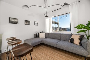 A modern living room with a grey sectional sofa, a large window with a view, and a plant.
