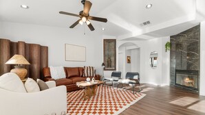 Un salon spacieux doté d’un plancher en bois, d’un ventilateur de plafond, d’une cheminée et d’une grande fenêtre.
