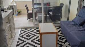 Ein modernes Wohnzimmer mit Sofa, Couchtisch und Essbereich mit Stühlen und Tisch. Ein Glastür öffnet sich zu einem Außenbereich mit Tisch und Stühlen.