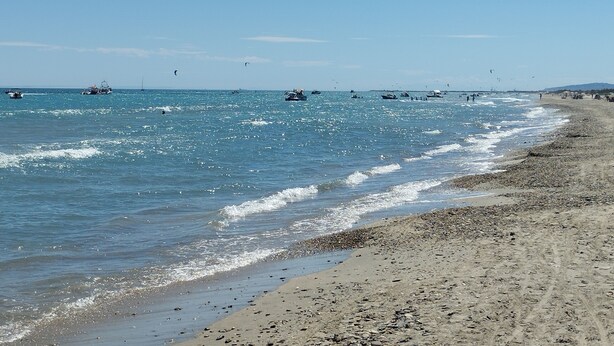 Ein Strand mit Booten, Menschen im Wasser und sandigem Ufer.