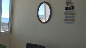 Ein Zimmer mit großem Fenster und Meerblick, einem runden Spiegel an der Wand und einem Motivationsschild mit einem Fahrrad und Text.