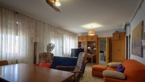 Ein Wohnzimmer mit Esstisch aus Holz, blau-orangefarbenen Sofas, einem Fernseher und Holzschränken.