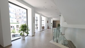 Un interior espacioso y moderno con un área amplia, una escalera con barandillas de vidrio y plantas en macetas.