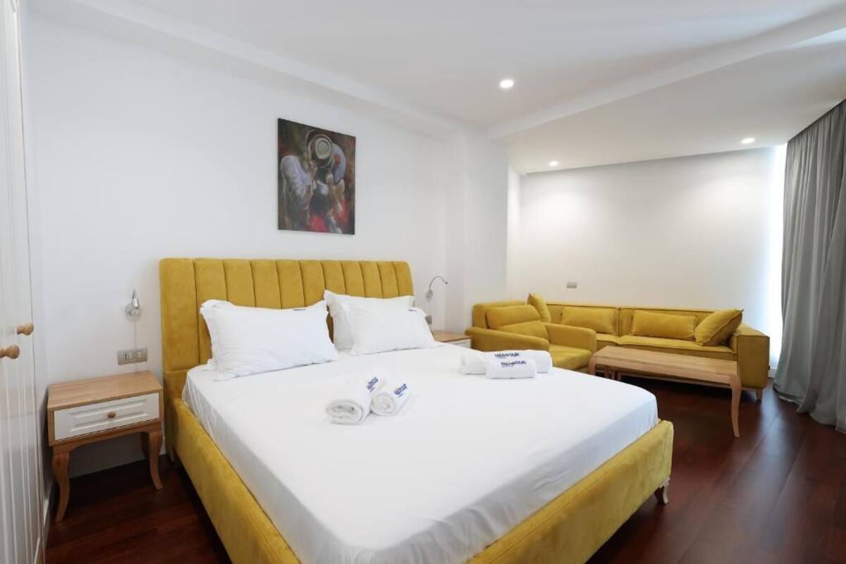 A hotel room with a large bed, a yellow sofa, and a painting on the wall.
