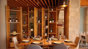 Un comedor con una mesa de madera dispuesta para cuatro personas, rodeada de sillas modernas. Se observan estantes con botellas de vino y objetos decorativos.