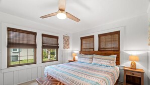 A bedroom with a bed, wooden headboard, two bedside tables with lamps, a bench, and a ceiling fan. - Adorable Laguna Beach Cottage with Pool, 1-Minute Walk to the Beach (Panama City Beach)