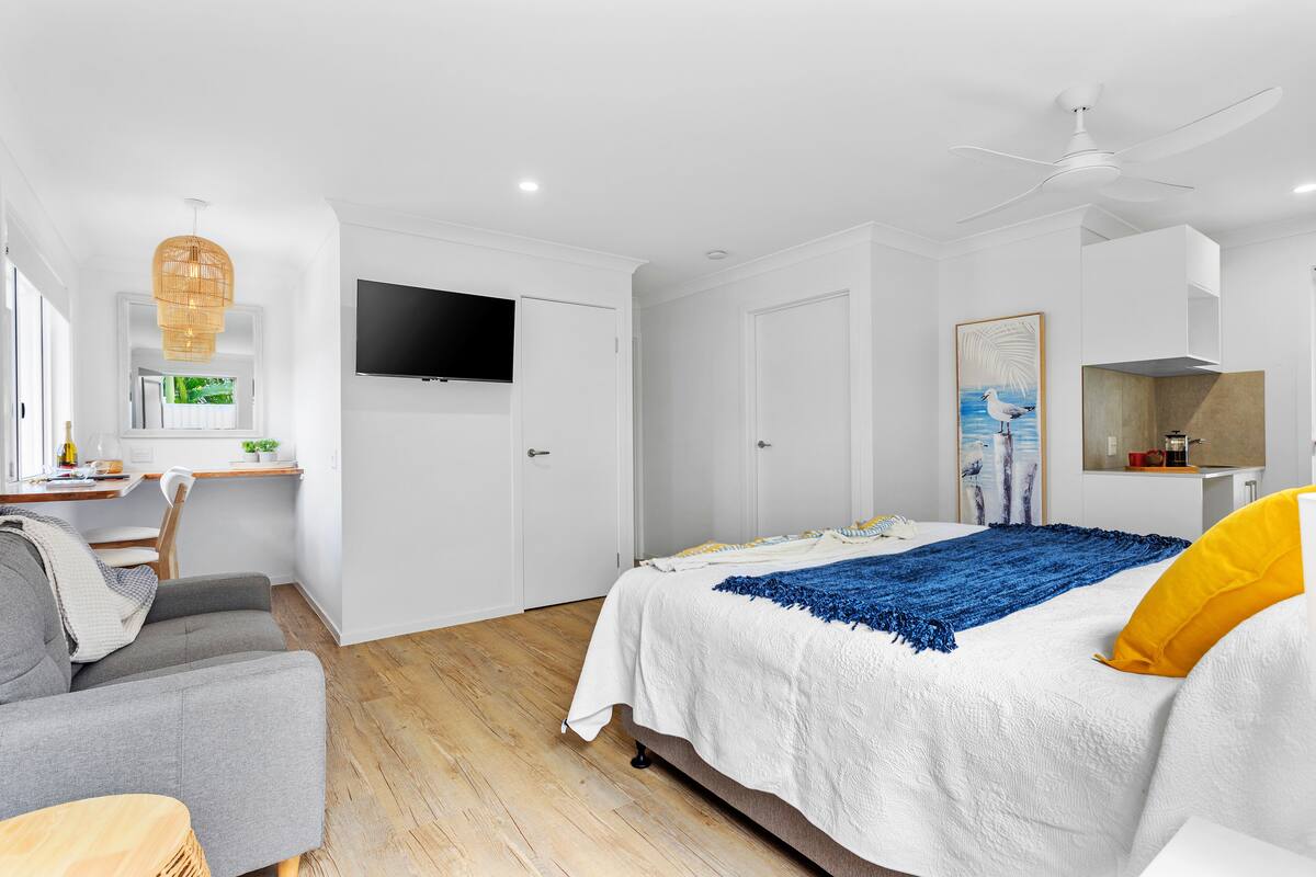 A modern bedroom with a bed, a desk, a chair, and a television.