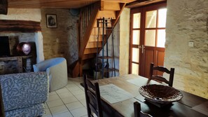 A rustic interior with a wooden staircase, a dining table with a placemat, and a patterned sofa.