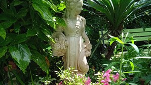 Uma estátua de jardim rodeada por vegetação exuberante e flores cor-de-rosa.