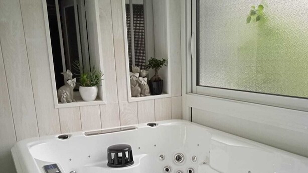 Uma casa de banho moderna com uma banheira branca, uma janela com vidro jateado e objetos decorativos no parapeito.