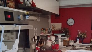 Cozinha com micro-ondas, forno e pia. Há um relógio na parede e uma parede vermelha.