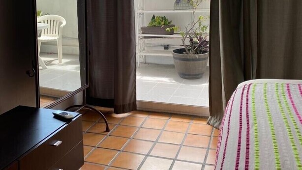 A bedroom with a bed, a dresser, and a balcony with potted plants. - Romantic Zone 5 Blocks From the Beach (Puerto Vallarta)