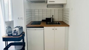 Eine kleine Küche mit weißen Schränken, einer schwarzen Arbeitsplatte, einem Geschirrspüler von Bosch, einem Spülbecken und einer Wanduhr.