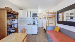A compact kitchen with white cabinets, a microwave, and a coffee maker. There is a wooden table and a bunk bed with a yellow pillow. - Functional studio, ski-in/out, south terrace (La Rosière)