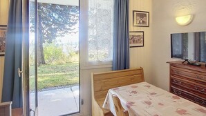 A bedroom with a bed, a dresser, a television, and a sliding glass door leading to a garden. - Functional studio, ski-in/out, south terrace (La Rosière)