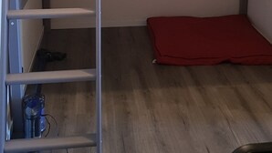 A bunk bed with a ladder, a red cushion, and a water bottle on the floor.