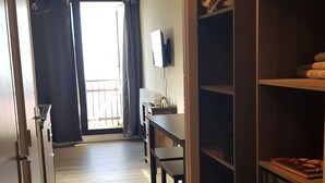 A narrow hallway with a wooden floor, a desk with a chair, a television, and a large wardrobe with shelves.