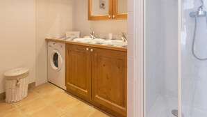 A compact bathroom with a washing machine, wooden cabinets, a sink, and a shower enclosure. - Spacious bright apartment at the slopes with parking (La Rosière)