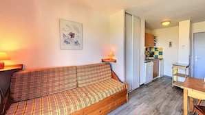 En hyggelig stue med en sofa, et lille bord og et køkken i baggrunden.