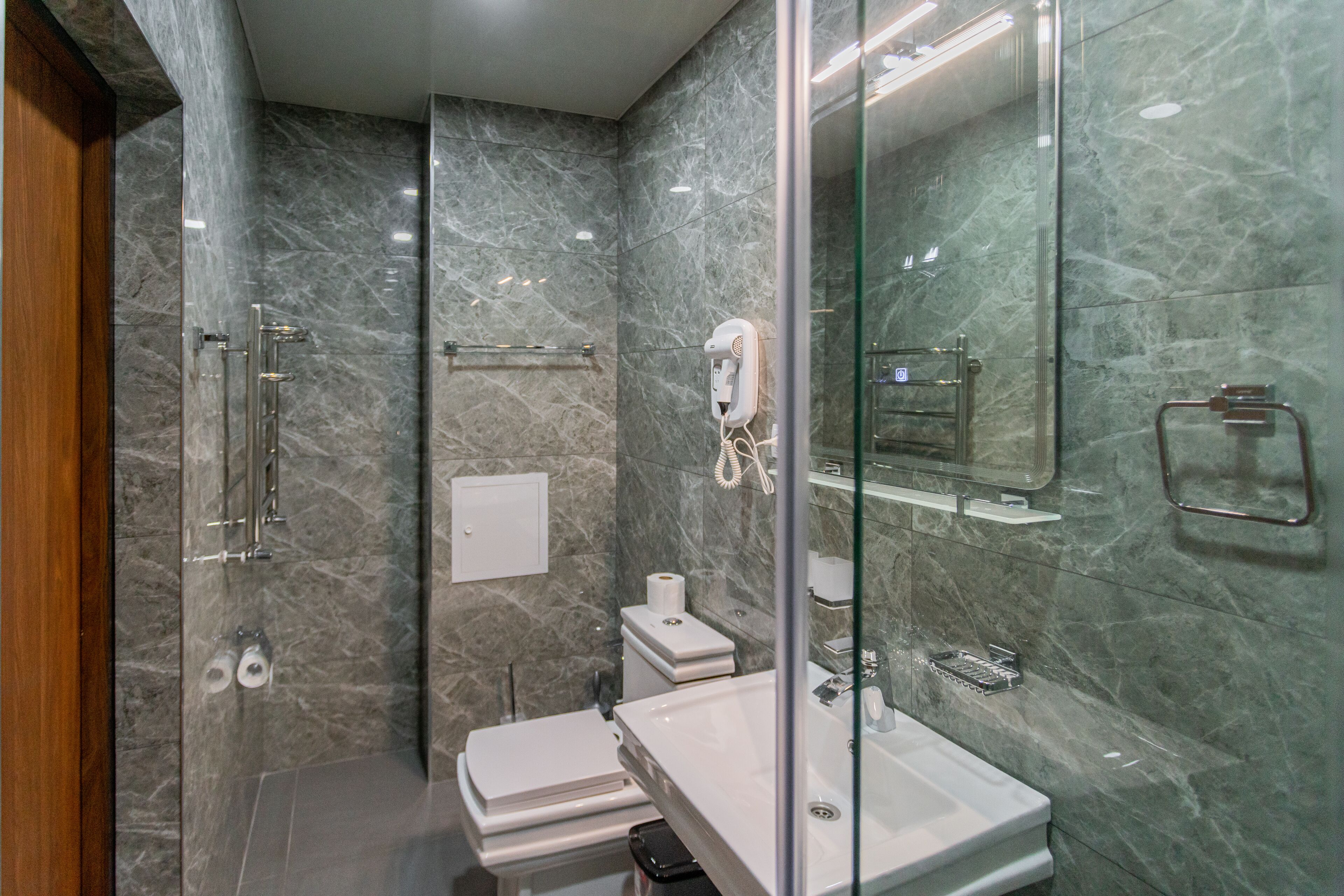 A modern bathroom with a glass shower enclosure, a white sink, and a marble-tiled wall.