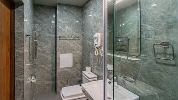 A modern bathroom with a glass shower enclosure, a white sink, and a marble-tiled wall.