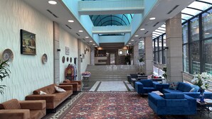 Een ruime lobby met een hoge plafond, een centrale trap en zithoeken met een patroonrijk tapijt.