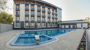 Een modern hotel met een gebogen gevel, een zwembad en een tuin met bloemen.