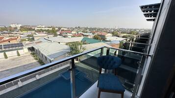 Varanda com guarda-corpo de vidro, vista para área residencial com diversos edifícios e céu claro.