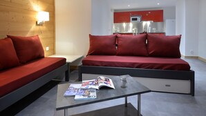 En moderne stue med en sofa og et sofabord, et køkken i baggrunden, og et magasin på bordet.
