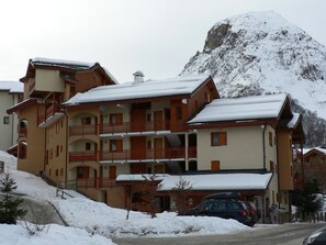 Un hôtel à plusieurs étages, doté de balcons, entouré d’un paysage enneigé et avec une montagne en toile de fond.