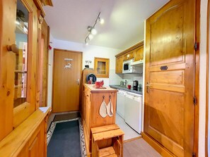 A compact kitchen with wooden cabinets, a microwave, a sink, and a small wooden stool.