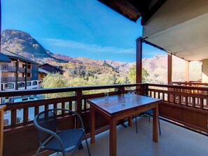A balcony with a wooden table and chairs, overlooking a mountainous landscape with buildings in the background. - Bright Spacious Apartment · Near Slopes · Balcony · Free Wi-Fi (Saint-Martin-de-Belleville)