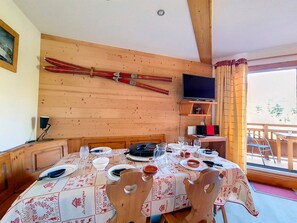 A dining area with a wooden table set for four, a television mounted on the wall, and a window with curtains. - Bright Spacious Apartment · Near Slopes · Balcony · Free Wi-Fi (Saint-Martin-de-Belleville)