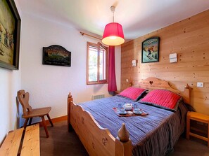 Ein Zimmer aus Holz mit einem Bett, einem Sessel, einem Tisch und einem Fenster.