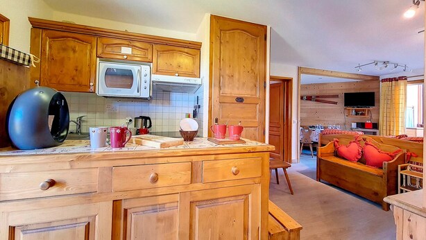 A kitchen with wooden cabinets, a microwave, and a coffee machine. There is a dining area with a wooden table and chairs. - Bright Spacious Apartment · Near Slopes · Balcony · Free Wi-Fi (Saint-Martin-de-Belleville)