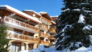 A multi-story hotel with balconies, surrounded by snow-covered trees. - Bright Spacious Apartment · Near Slopes · Balcony · Free Wi-Fi (Saint-Martin-de-Belleville)