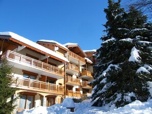 Un hôtel à plusieurs étages, doté de balcons et entouré d’arbres couverts de neige.