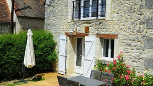 Une maison en pierre avec une terrasse en bois, une table et des chaises.
