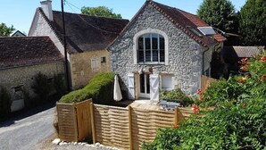 Une maison en pierre avec un toit en pente, une clôture en bois et un jardin parsemé de fleurs rouges.