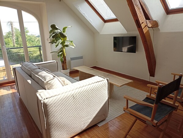A modern loft bedroom with a large window, a sofa, a wooden table, and a chair.