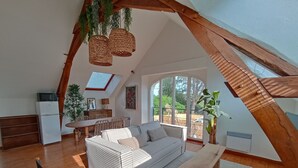A spacious loft with a high ceiling, a dining area, a sofa, a wooden bench, and a kitchen area with a refrigerator and microwave. - Ancien Studio D'artiste à la Campagne (Vou)