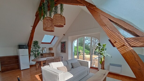 Un loft spacieux avec un plafond haut, un coin repas, un canapé, un banc en bois et un coin cuisine équipé d’un réfrigérateur et d’un four à micro-ondes.