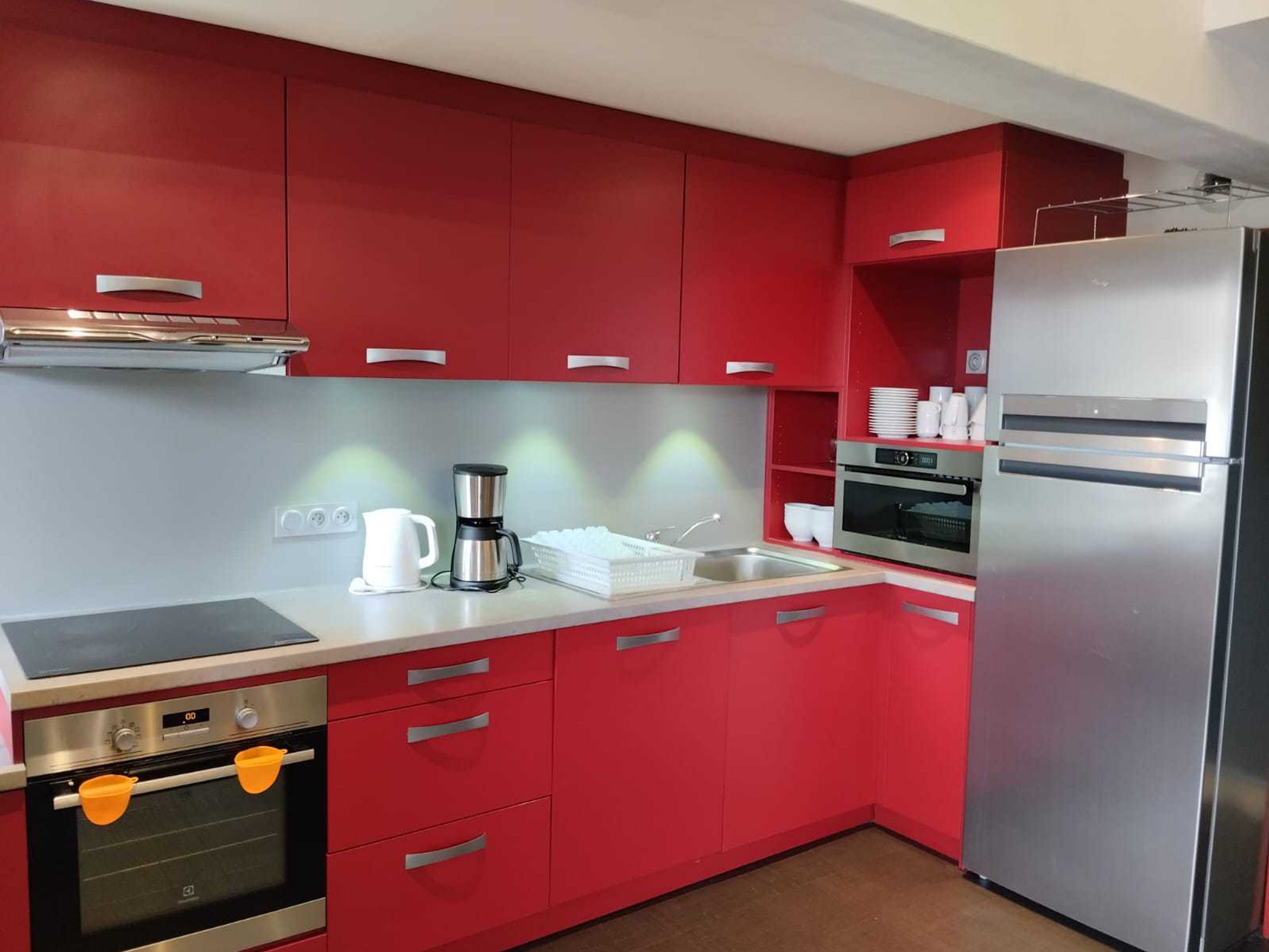 Een moderne keuken met rode kastjes, roestvrijstalen apparatuur en een wit aanrecht.