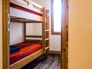 Ein Schlafraum mit Etagenbetten, einem Holzrahmen, einer roten Matratze und einem Fenster mit Blick nach draußen.