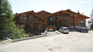 Edificio in legno a più piani con balconi, un'area parcheggio e una persona che cammina.