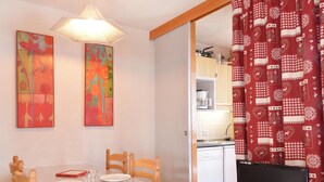A dining area with a table set for two, a television on a stand, and a kitchen visible through an open door. - Bright studio near slopes with balcony - Pets allowed (Plagne Bellecôte)