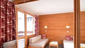 A cozy room with a wooden interior, a sofa, a small table, and a television. - Bright studio near slopes with balcony - Pets allowed (Plagne Bellecôte)