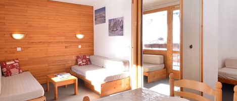 A cozy room with a wooden wall, a sofa, a small table, and a dining area with chairs and a table set for two.