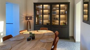 Un coin repas avec une table en bois, des sets de table en fibres tressées et des chaises. Une vitrine aux portes en verre expose divers objets.